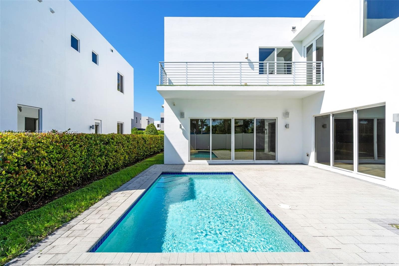 Contemporary exterior featuring a private swimming pool, concrete paver patio, second-story balcony with metal railing, and expansive glass sliding doors