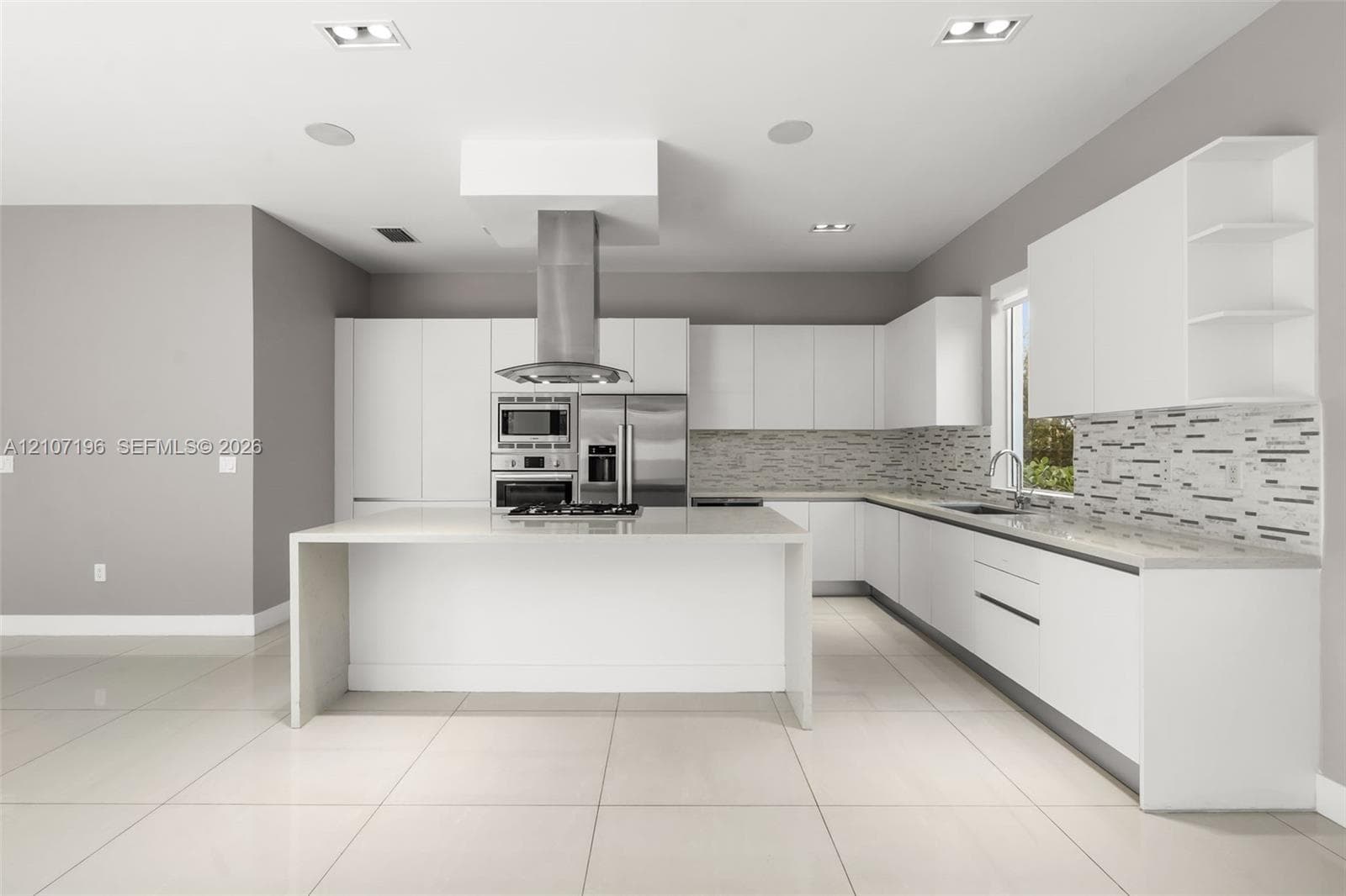 Kitchen featuring flat-panel cabinetry, a central island with a waterfall countertop, stainless steel appliances, a linear-patterned backsplash, and light-toned tile flooring