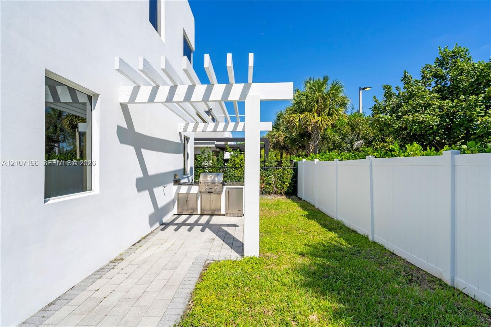Outdoor space featuring a white pergola, built-in stainless steel grill, stone-paver patio, and white vinyl privacy fencing