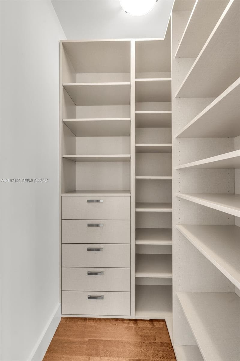 Customized built-in storage system featuring floor-to-ceiling shelving, five soft-close drawers with metallic pulls, and wood-finish flooring