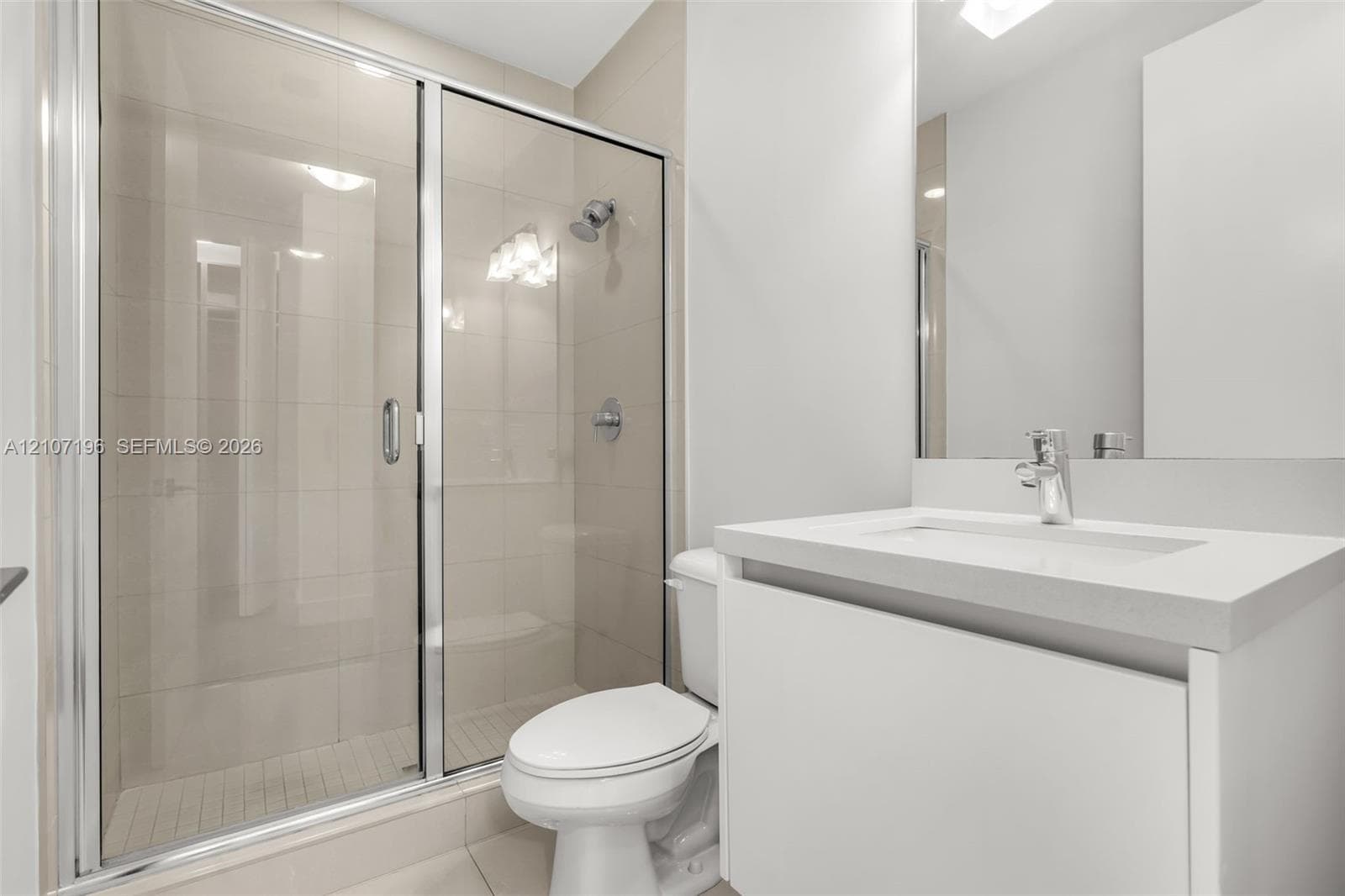 Bathroom featuring a sliding glass shower door, floor-to-ceiling wall tile, white vanity with a solid-surface countertop, and a built-in mirror