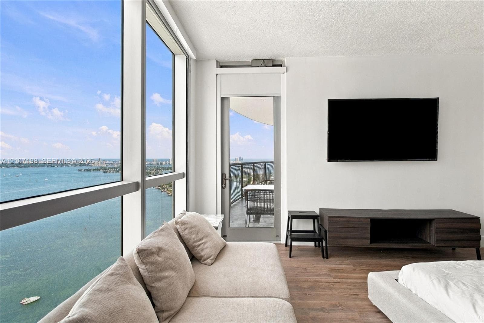 Matte black cabinetry, stone-finish countertops, stainless steel appliance suite, wood-finish flooring, and a private balcony with water backdrop