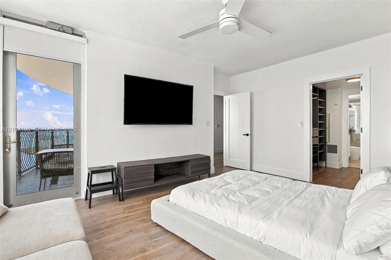 Floor-to-ceiling windows, wood-finish flooring, balcony with metal railing, and a dark vertical-slat accent wall