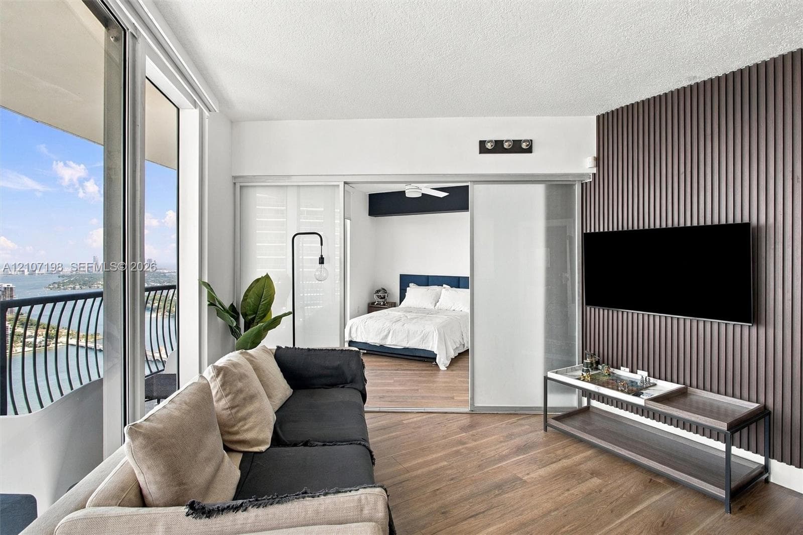 Floor-to-ceiling windows, wood-finish flooring, sliding glass door access to a private balcony, and metal balcony railing