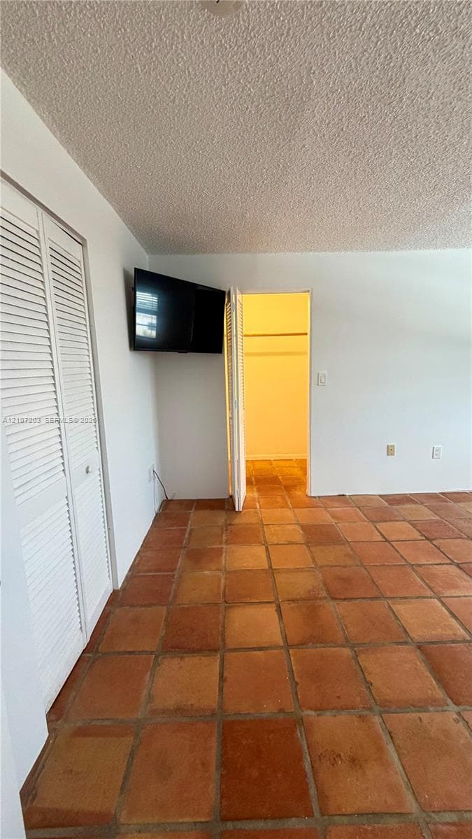 Room featuring terra-cotta tile flooring, white walls, and bi-fold closet doors