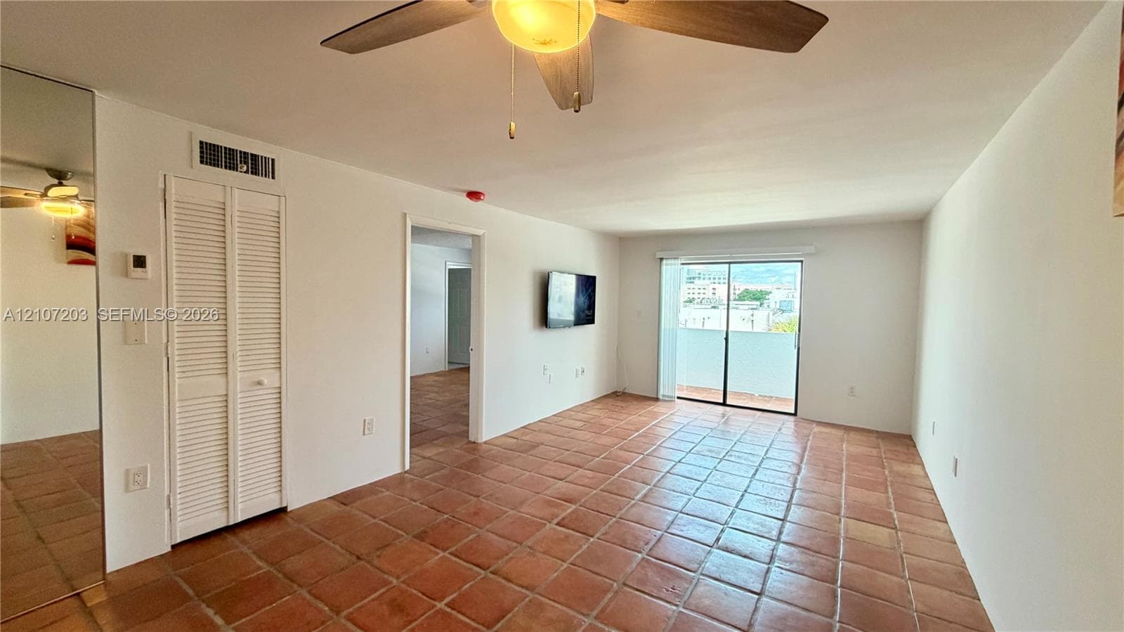 Interior space featuring tile flooring, mirrored wall paneling, a ceiling fan with integrated lighting, and sliding glass doors with balcony access