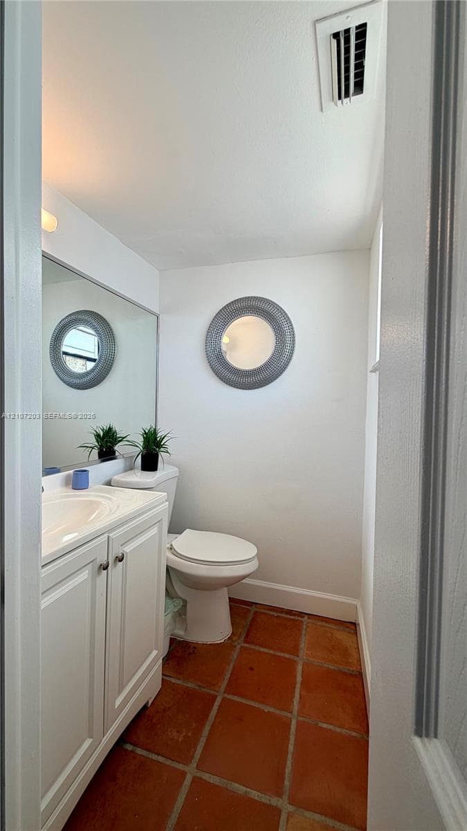 Bathroom featuring terra cotta tile flooring, white cabinetry with an integrated basin, a large wall-mounted mirror, and circular decorative wall accent