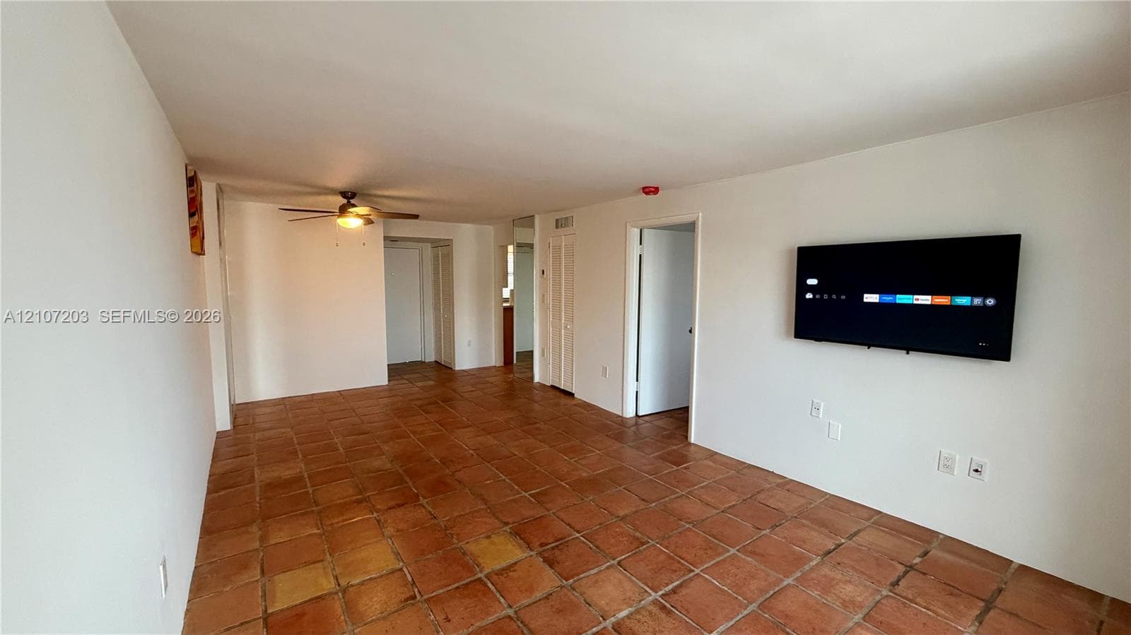 Interior space featuring terra-cotta tile flooring, white walls, and a ceiling-mounted fan with integrated light fixture