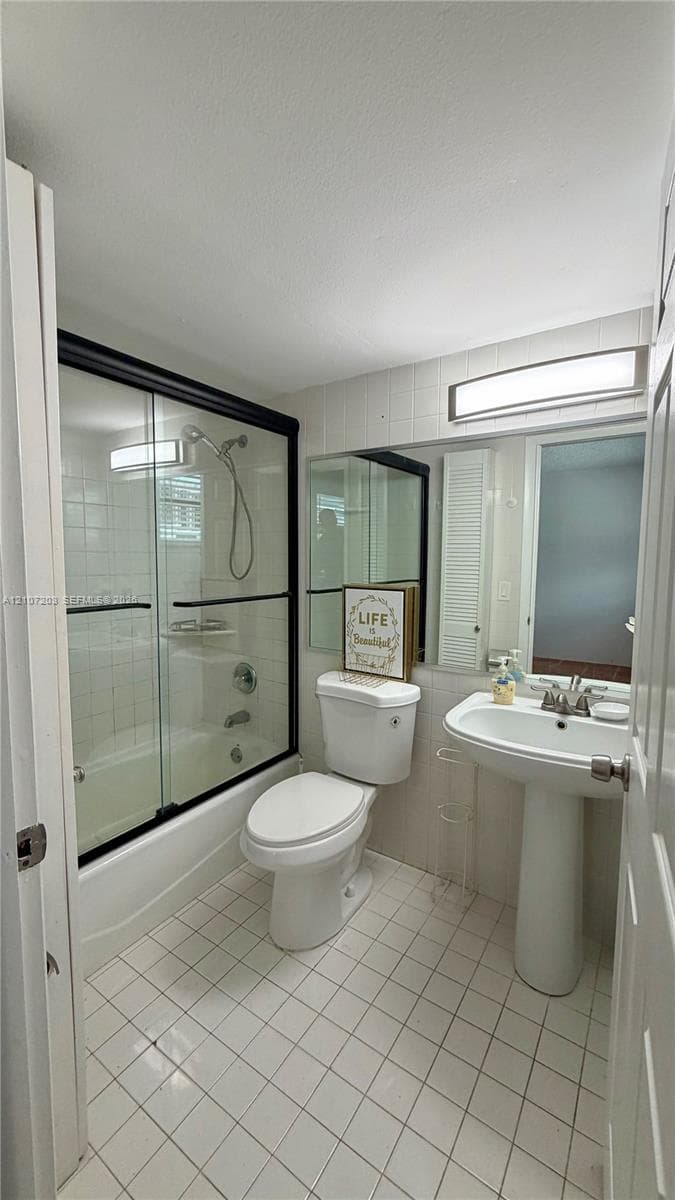 Bathroom featuring a pedestal sink, tub with a glass sliding door enclosure, handheld shower fixture, and square tile flooring