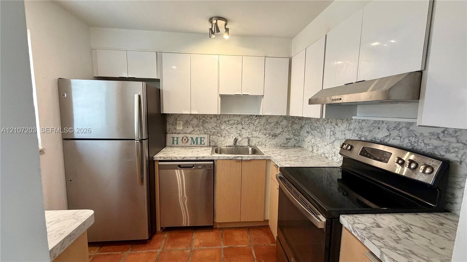 Kitchen featuring white high-gloss cabinetry, stone-patterned laminate countertops, stainless steel appliances, a mounted range hood, and terracotta tile flooring