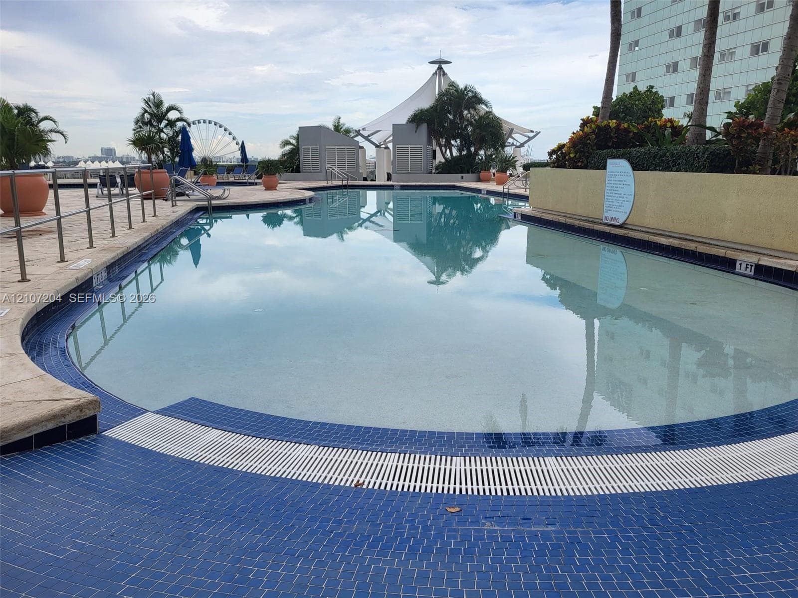 Swimming pool featuring blue tile decking, metal perimeter railings, and landscaping