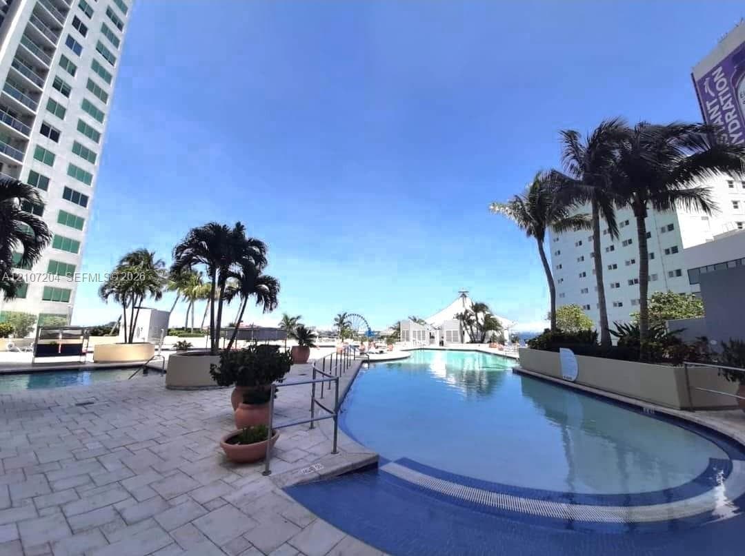 Swimming pool with a tile perimeter and tiered steps, surrounded by a paved deck, built-in planters, and mature palm trees