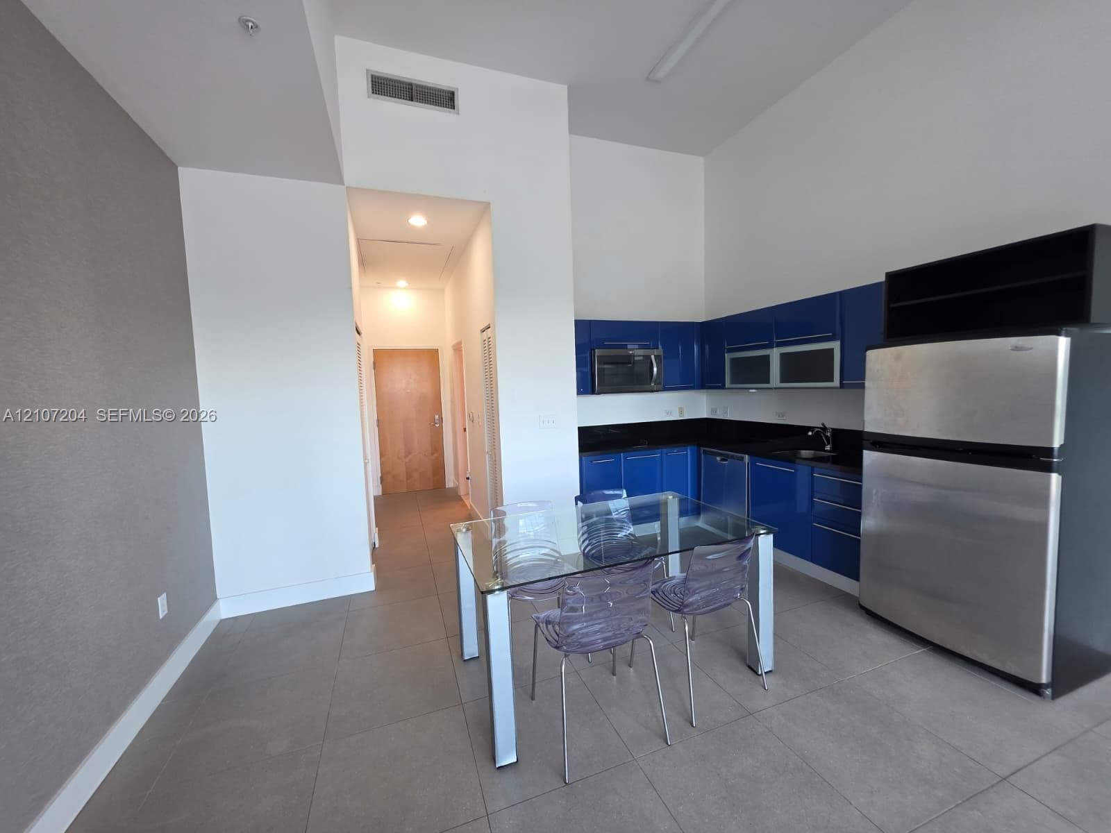 Kitchen featuring high-gloss blue cabinetry, dark solid-surface countertops, stainless steel appliances, large-format tile flooring, and high ceilings