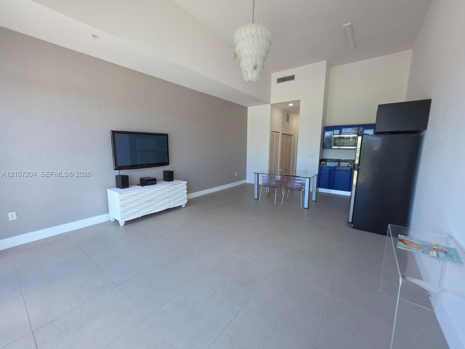 Open-concept interior featuring large-format tile flooring, vaulted ceilings, and a statement chandelier