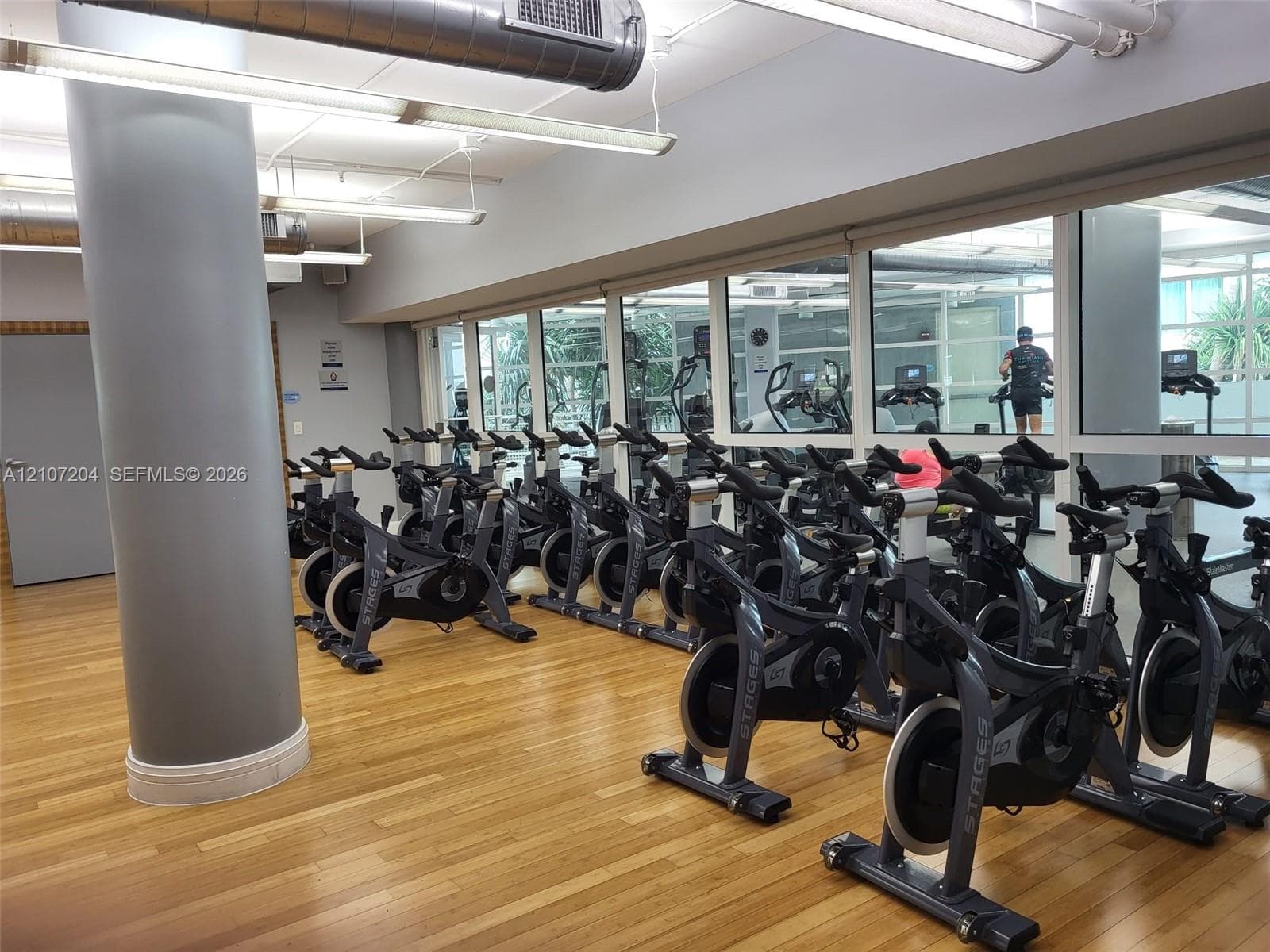 Fitness room featuring wood-finish flooring, floor-to-ceiling mirrored walls, industrial exposed ductwork, and large windows