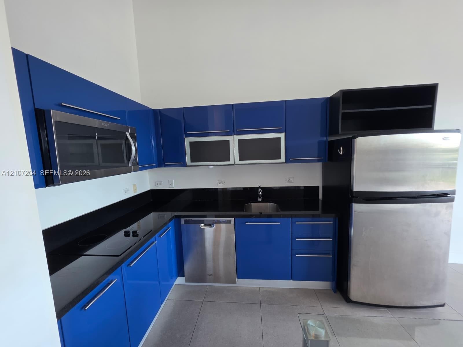 Kitchen featuring high-gloss blue cabinetry, black countertops, stainless steel appliances, and large-format tile flooring