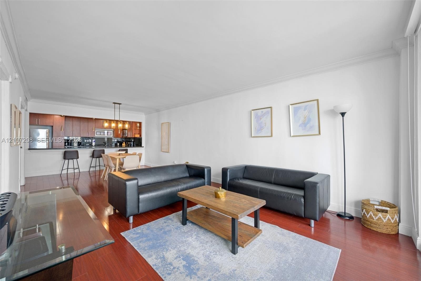 Open-concept interior featuring wood-finish flooring, crown molding, and a kitchen with wood-finish cabinetry, a breakfast bar, and a pendant light fixture