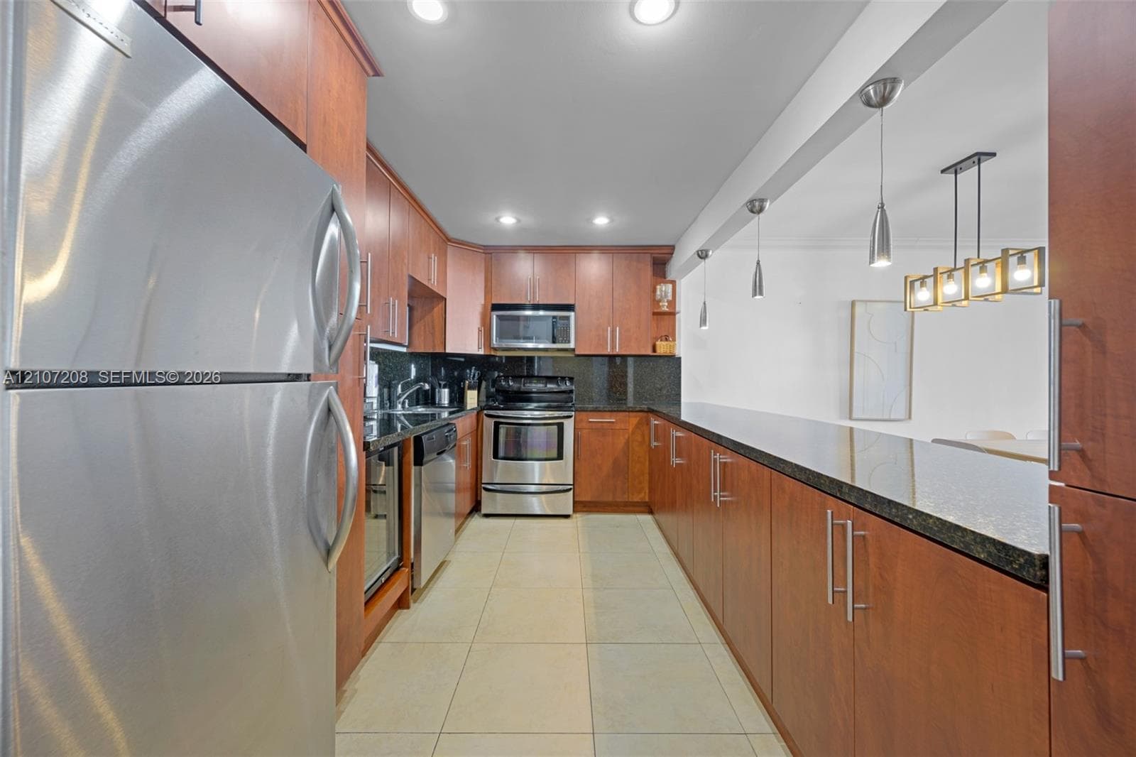 Kitchen featuring stainless steel appliances, dark stone countertops, custom wood-finish cabinetry, ceramic tile flooring, and integrated pendant lighting