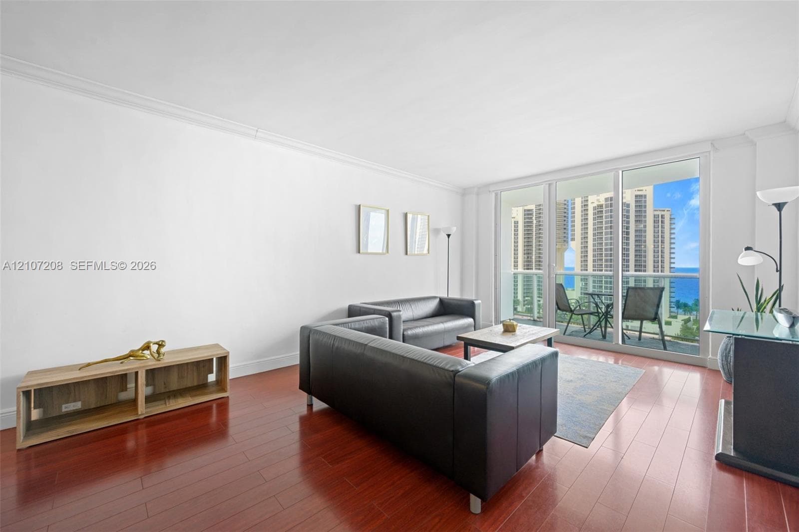 Living area featuring wood-finish flooring, crown molding, and floor-to-ceiling glass sliding doors opening to a balcony
