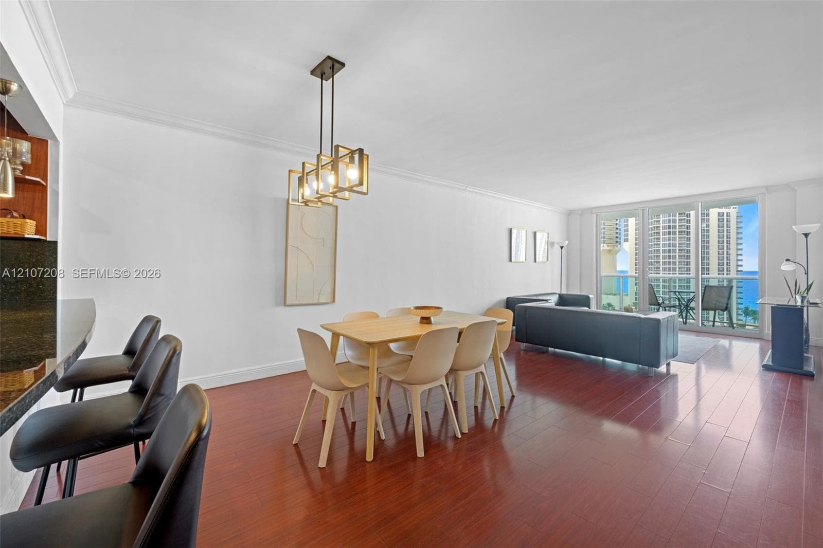 Open-concept interior featuring wood-finish flooring, a kitchen breakfast bar with stone-finish countertop, geometric pendant lighting, and large sliding glass doors providing outdoor access