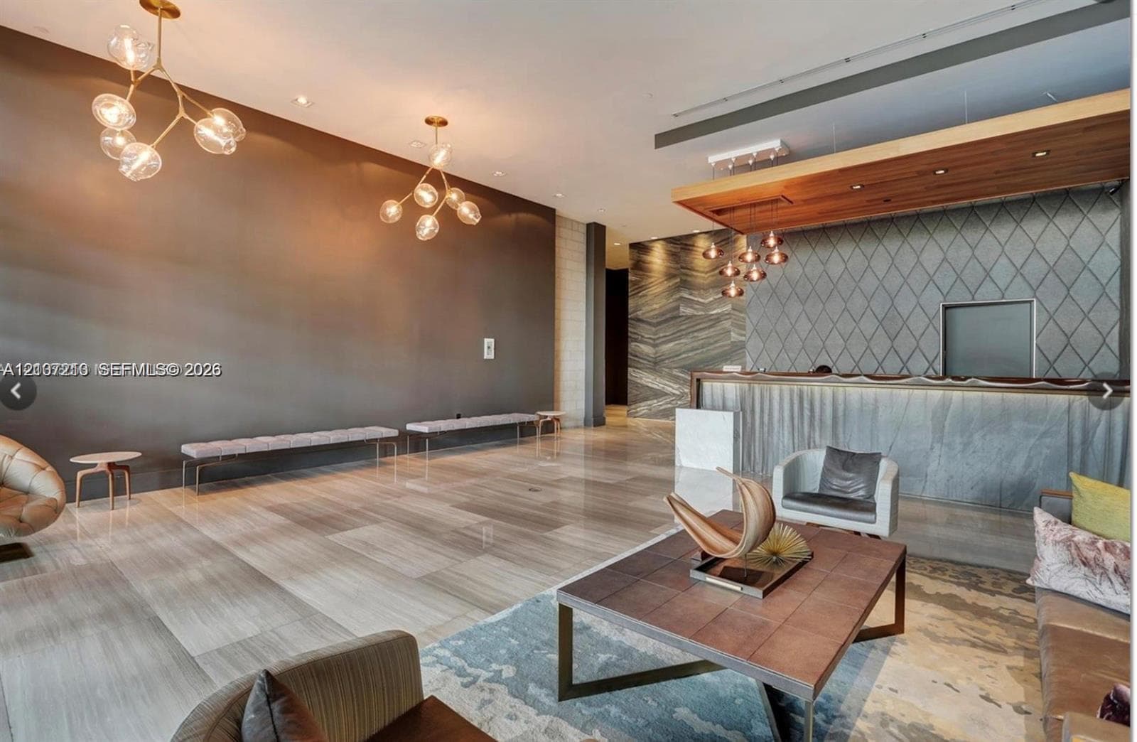 Large-format stone tile flooring, modern multi-globe pendant lighting, built-in reception desk with stone facade, decorative diamond-patterned wall paneling, and wood-finish ceiling accent