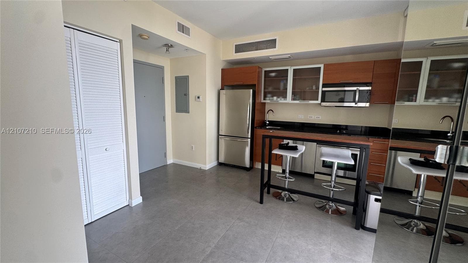 Kitchen featuring flat-panel wood-finish cabinetry, stainless steel appliances, dark stone countertops, glass-front upper cabinets, and tile flooring