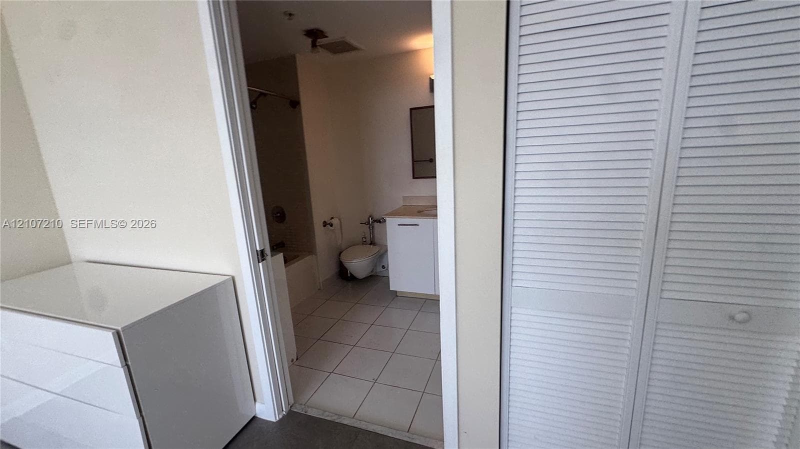Bathroom featuring white floor tiling, vanity with a light-toned countertop, and bi-fold louvered closet doors
