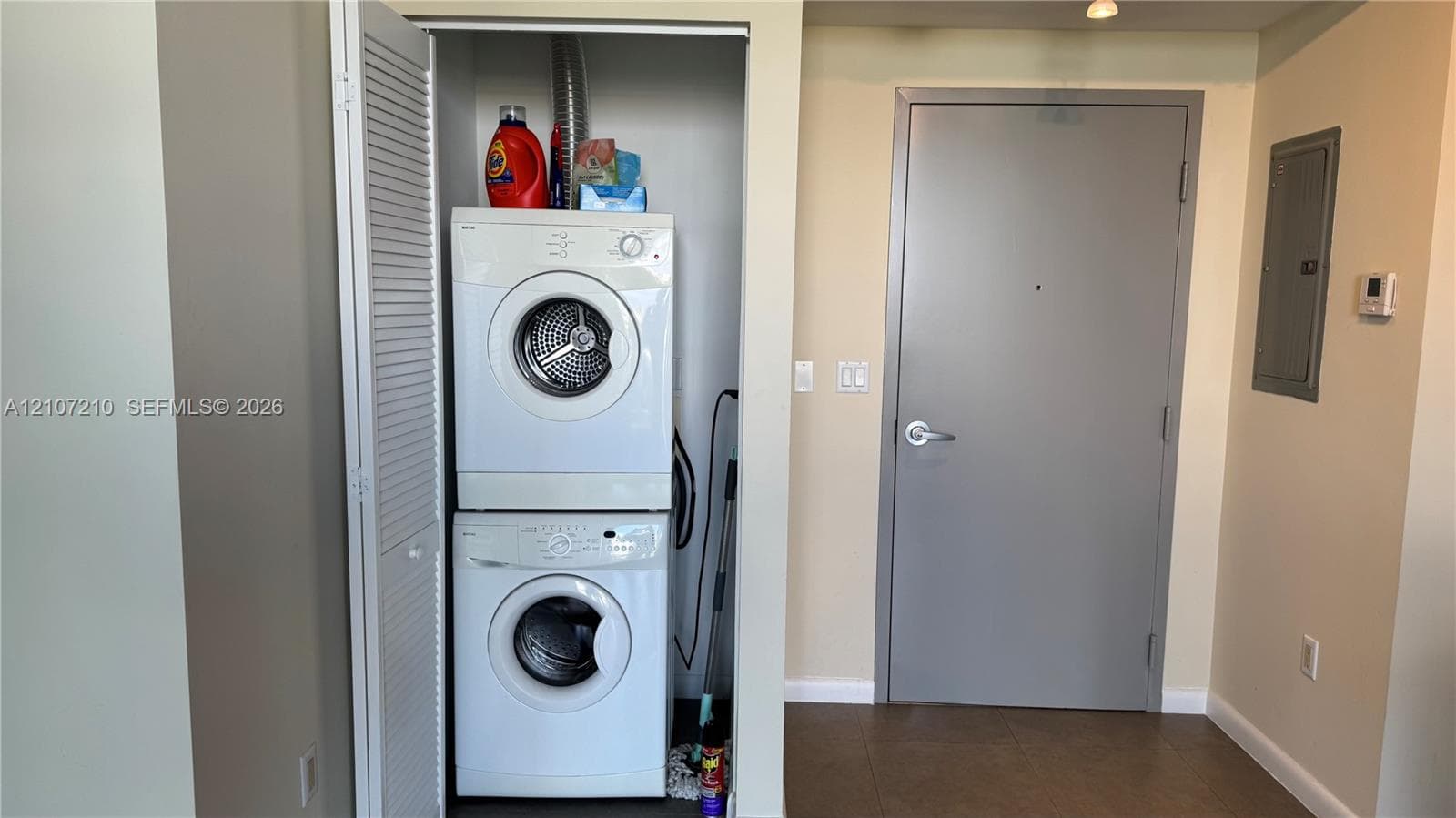 Stackable laundry unit housed in a dedicated closet with louvered doors, featuring a solid-core interior door and tile flooring