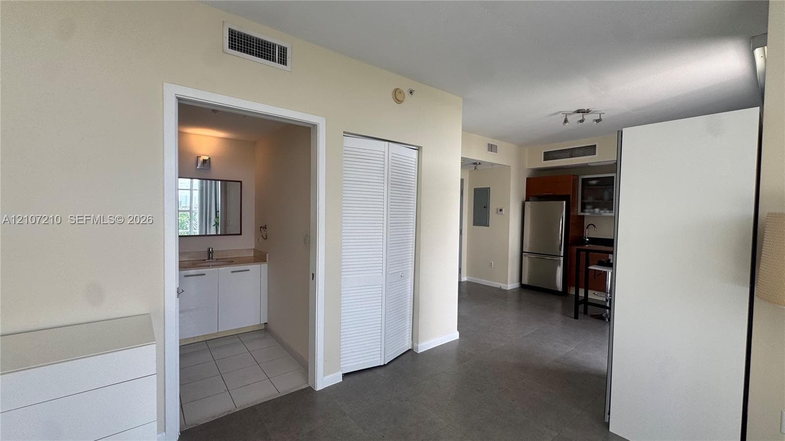 Interior space featuring large-format tile flooring, a kitchenette equipped with stainless steel appliances and cabinetry, and a bathroom containing a vanity with a solid-surface countertop and wall-mounted mirror