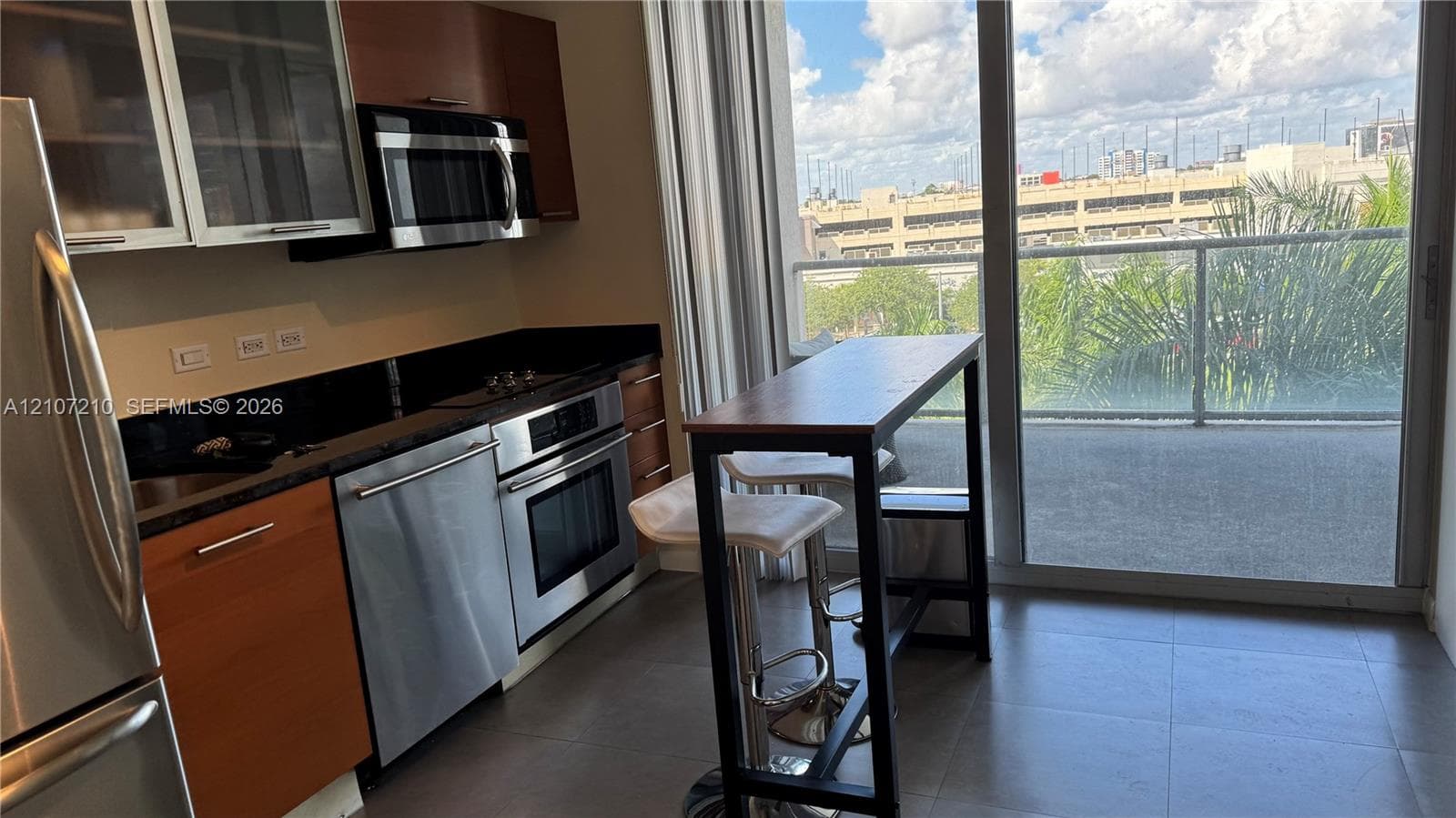 Kitchen featuring stainless steel appliances, flat-panel cabinetry, stone countertops, large-format tile flooring, and floor-to-ceiling sliding glass doors opening to a balcony