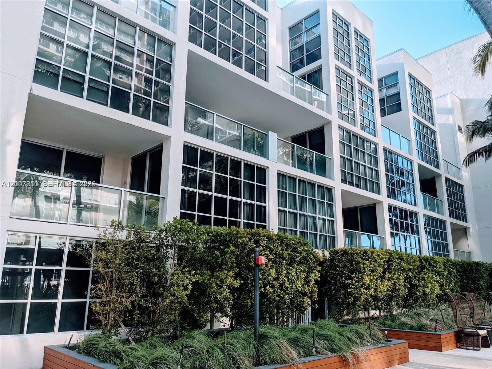 Modern mid-rise exterior featuring a multi-story glass grid facade, integrated private balconies, and raised planters with built-in wood-finish bordering