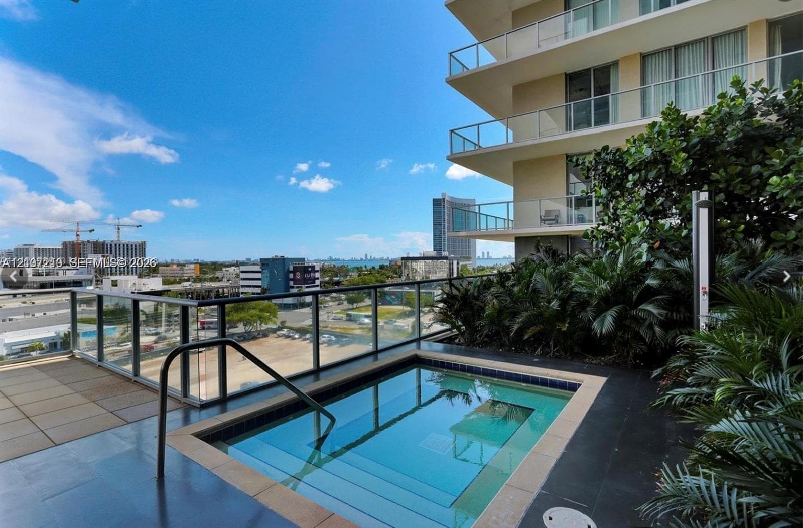 Elevated terrace featuring a built-in plunge pool, glass panel railings, tiled decking, and manicured perimeter landscaping