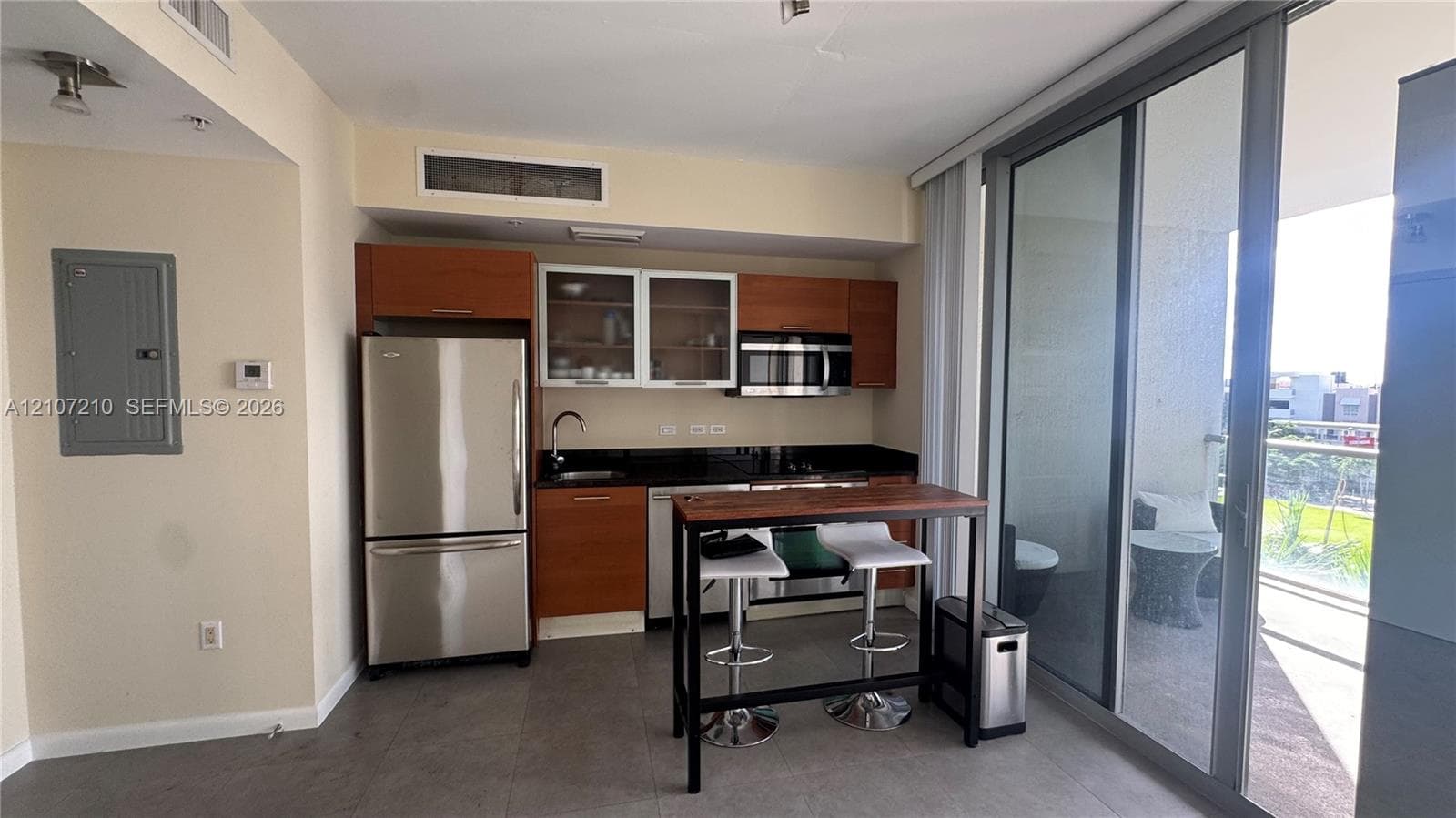 Kitchen featuring wood-veneer cabinetry, dark stone countertops, stainless steel appliances, and tile flooring, including full-height sliding glass doors
