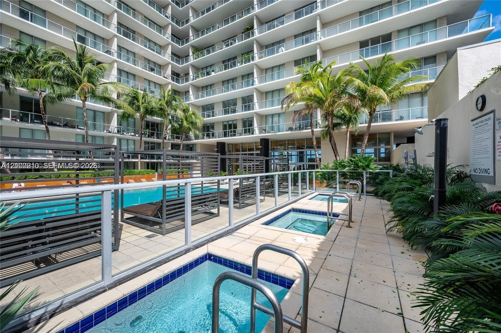 Resort-style pool area featuring multiple tiled spas, stone-paver decking, metal railings, and mature palm trees