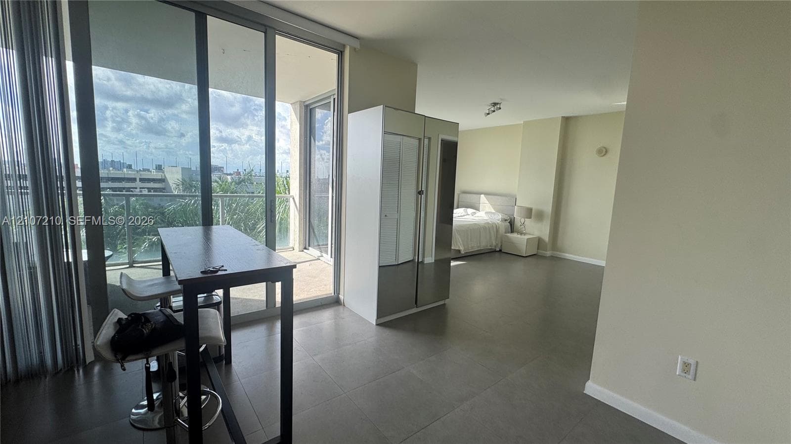 Open-concept interior featuring large-format tile flooring, floor-to-ceiling glass sliding doors, and a private balcony with metal railing