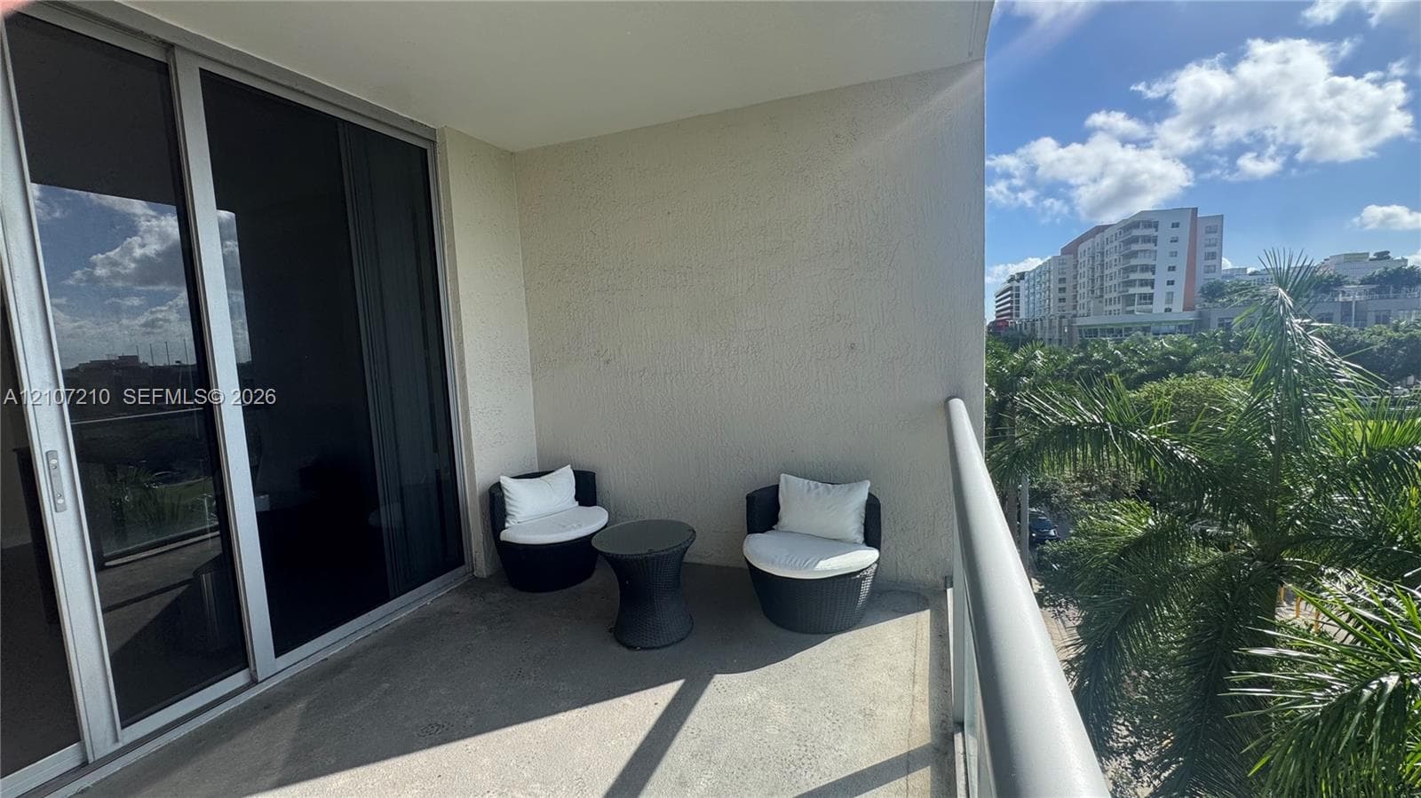 Covered balcony with a concrete floor, stucco wall finish, and metal railing, featuring oversized sliding glass doors