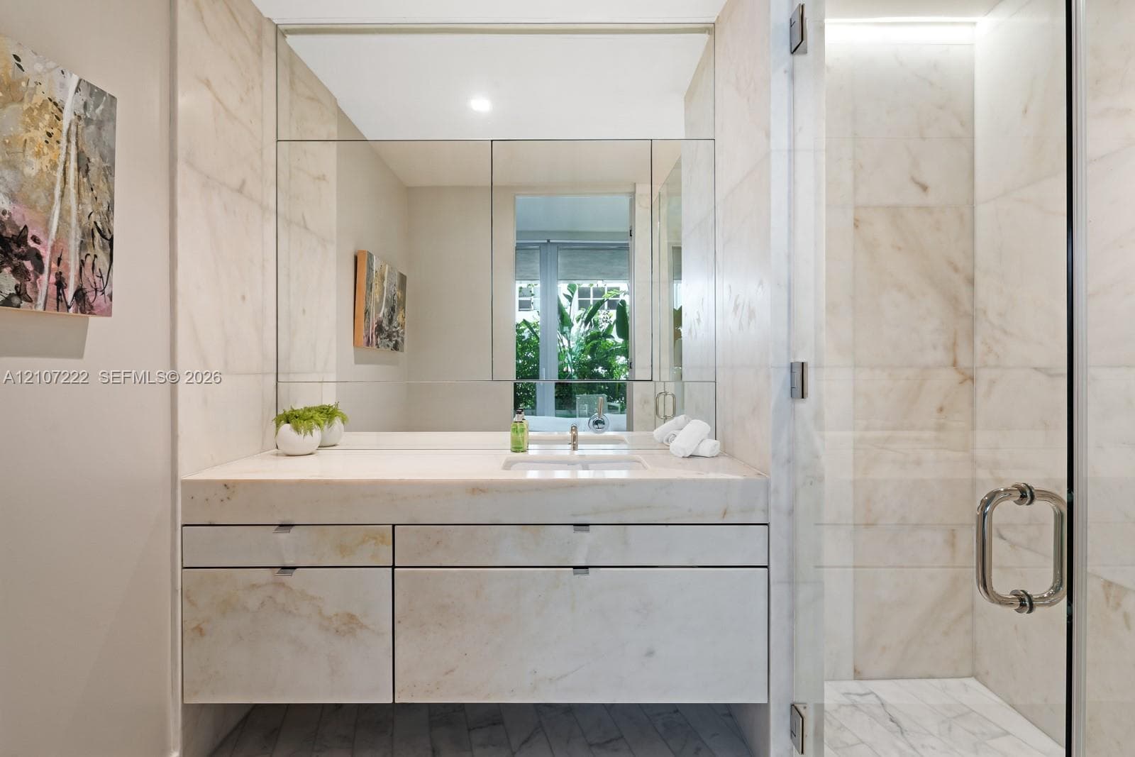 Floating vanity with stone-surfaced countertop, large-format tiled shower enclosure, glass entry door, and wall-to-wall mirror