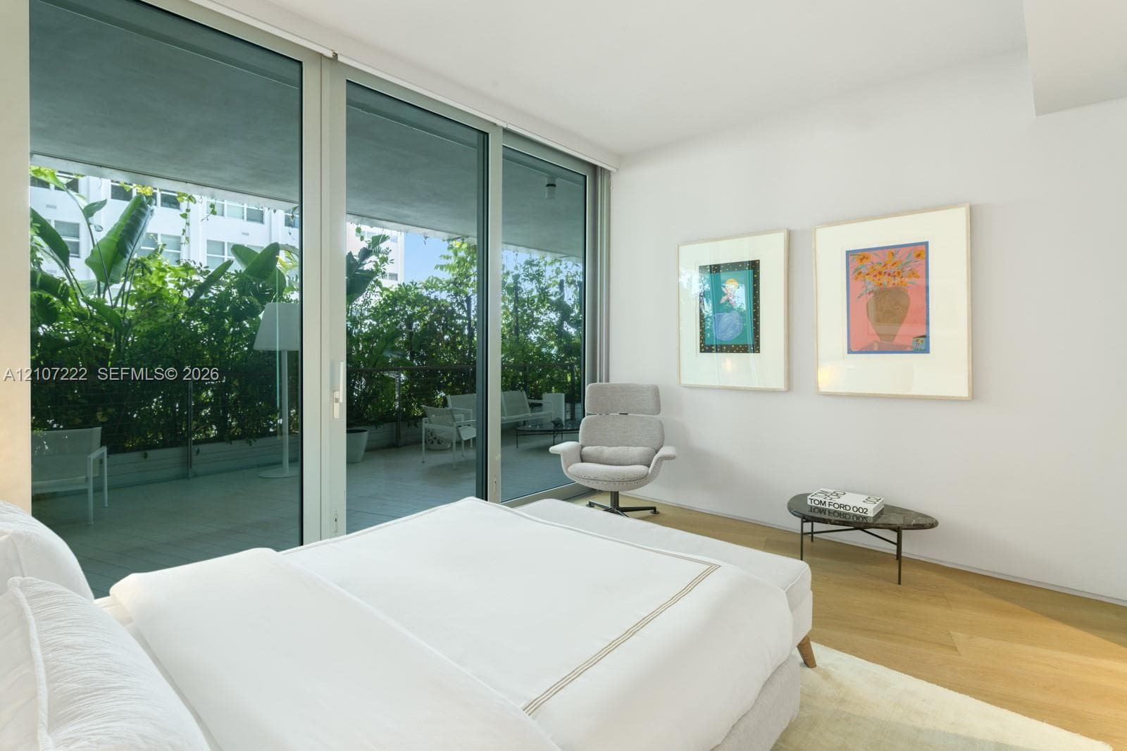Floor-to-ceiling glass sliding doors, private covered balcony with glass railing, and light-tone wood-finish flooring