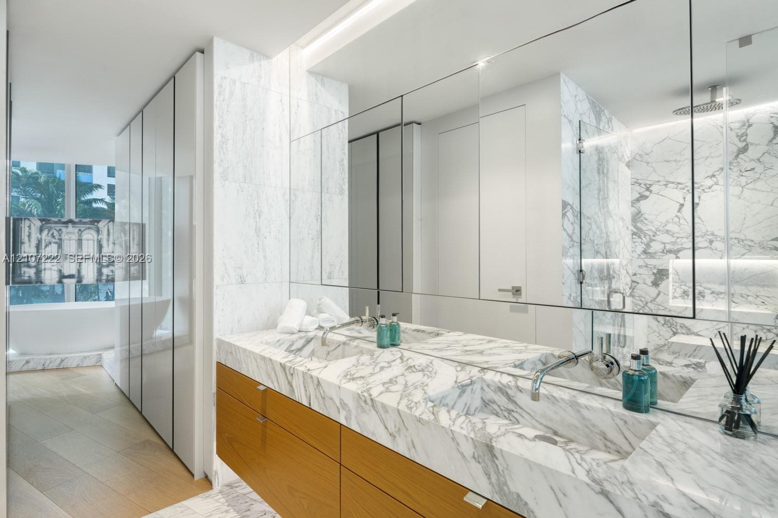 Double vanity with stone-surfaced integrated sinks and countertop, natural wood-finish cabinetry, floor-to-ceiling stone wall tiling, and glass-enclosed shower area