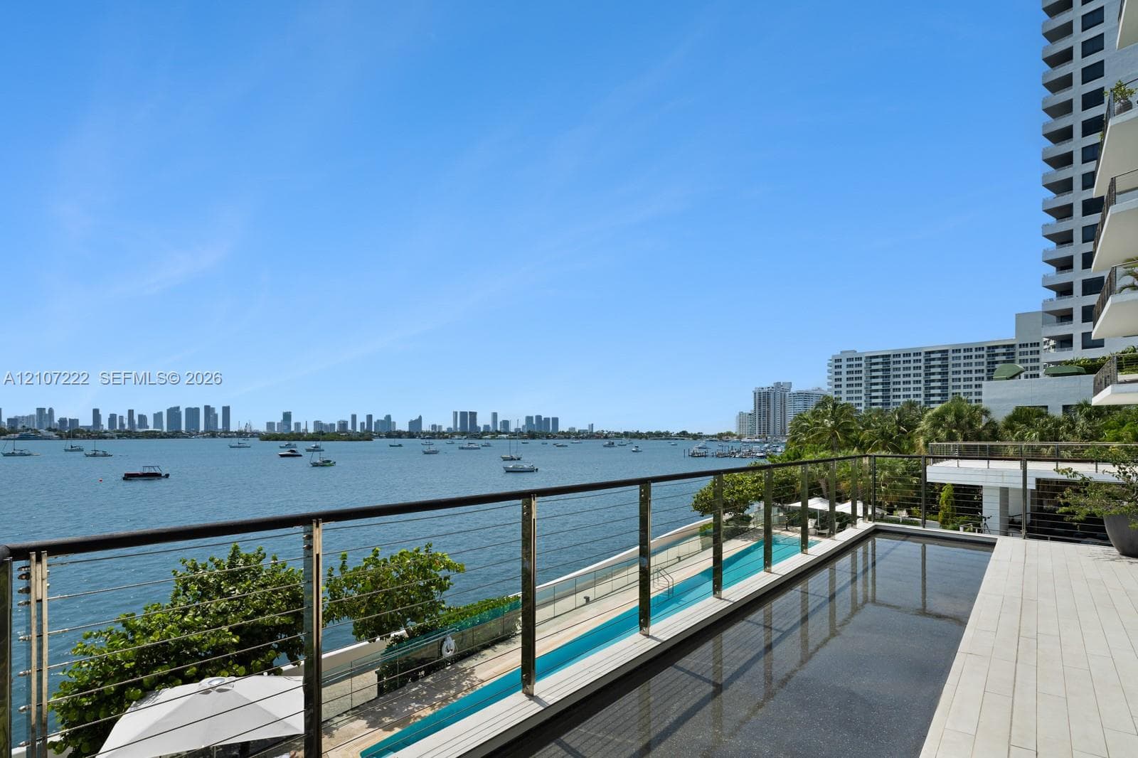 Elevated terrace featuring stone tile flooring, an infinity-edge pool, and a metal railing with horizontal wire cabling