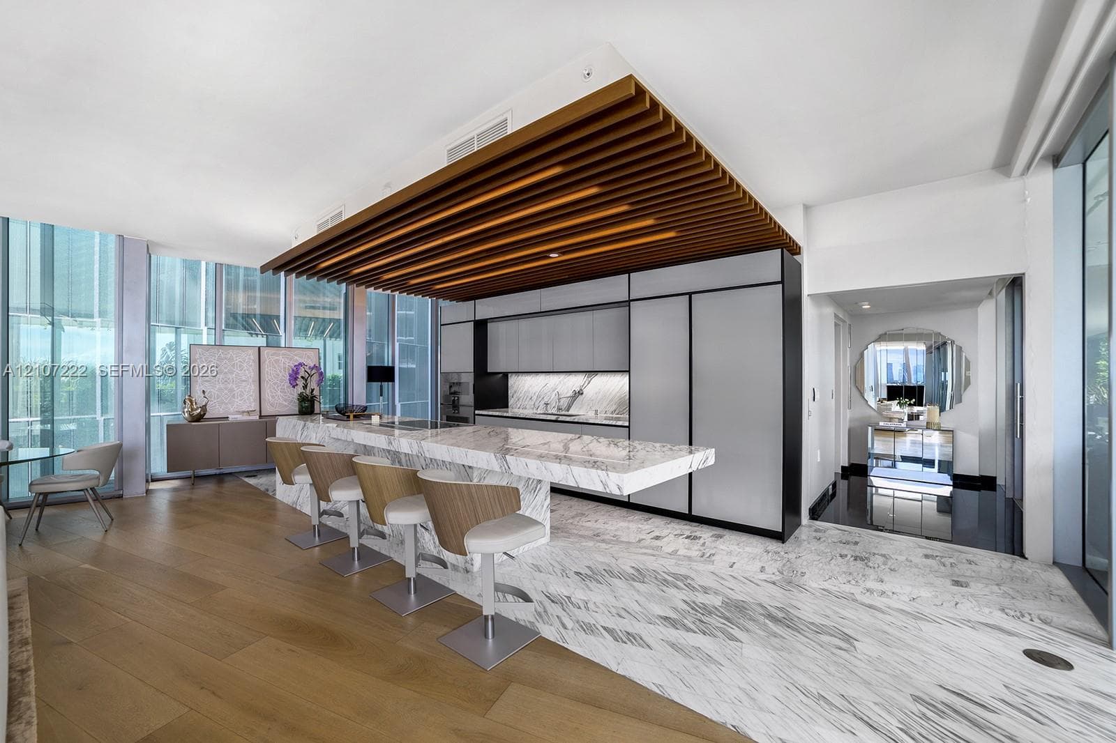 Gourmet kitchen featuring a stone-topped waterfall island, custom flat-panel cabinetry, integrated appliances, decorative wood slat ceiling detail, and mixed wood-finish and stone flooring