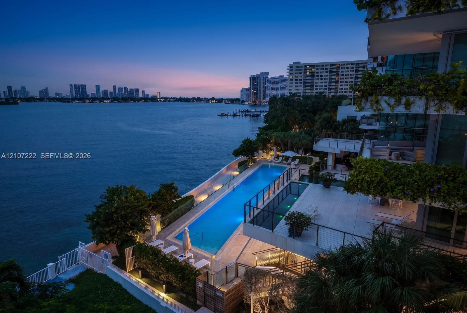 Waterfront property featuring a rectangular lap pool, expansive tiled terrace, tiered multi-level balconies, and glass panel railings