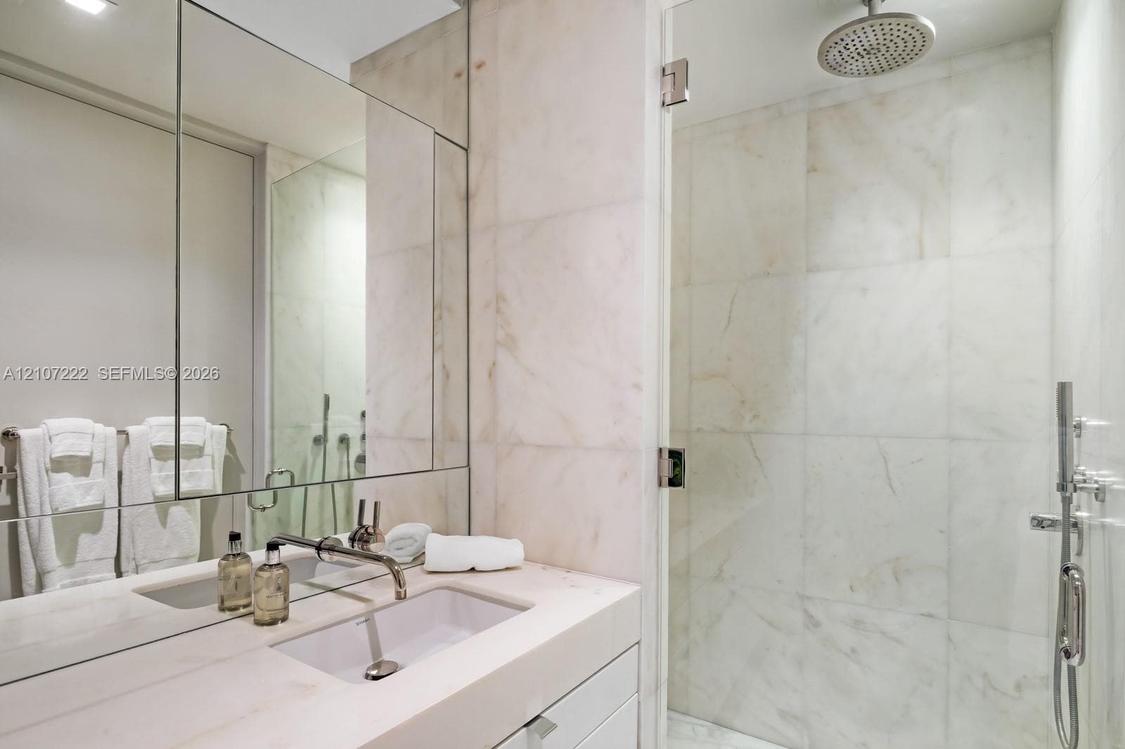 Bathroom featuring a floating vanity with a stone countertop and integrated sink, full-height wall mirror, stone-tile walk-in shower with a glass door, rainfall showerhead, and a hand-held shower sprayer
