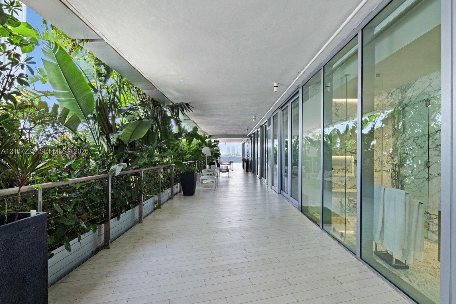 Expansive covered terrace featuring light-toned tile flooring, floor-to-ceiling glass panel walls, integrated railing, and built-in landscape planters