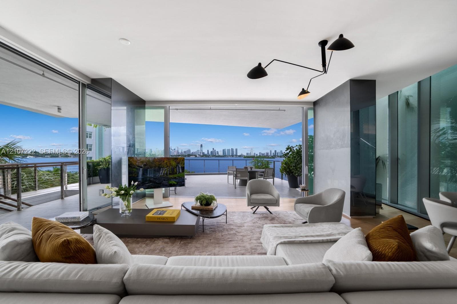 Expansive living space featuring floor-to-ceiling glass walls, integrated sliding door system, matte black multi-arm ceiling fixture, and deep covered balcony