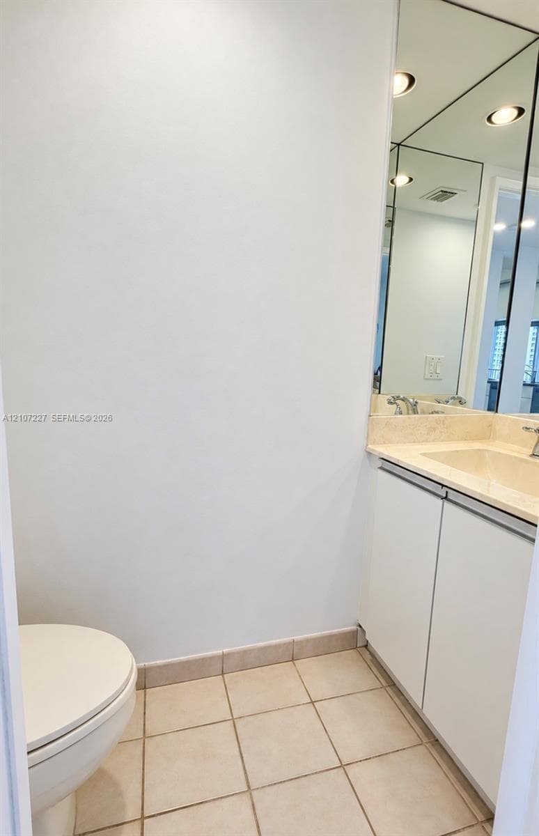 Bathroom vanity with stone-finish countertop, integrated sink, white cabinetry, tile flooring, and large wall-mounted mirror