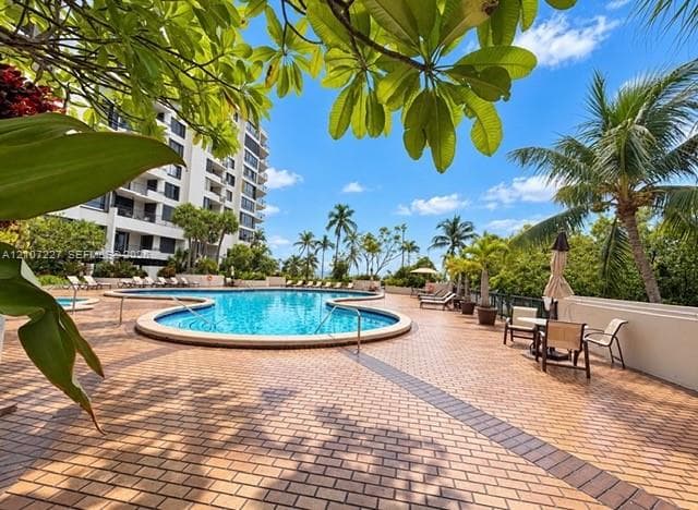 Curved swimming pool featuring brick paver decking, decorative metal railings, and mature tropical landscaping