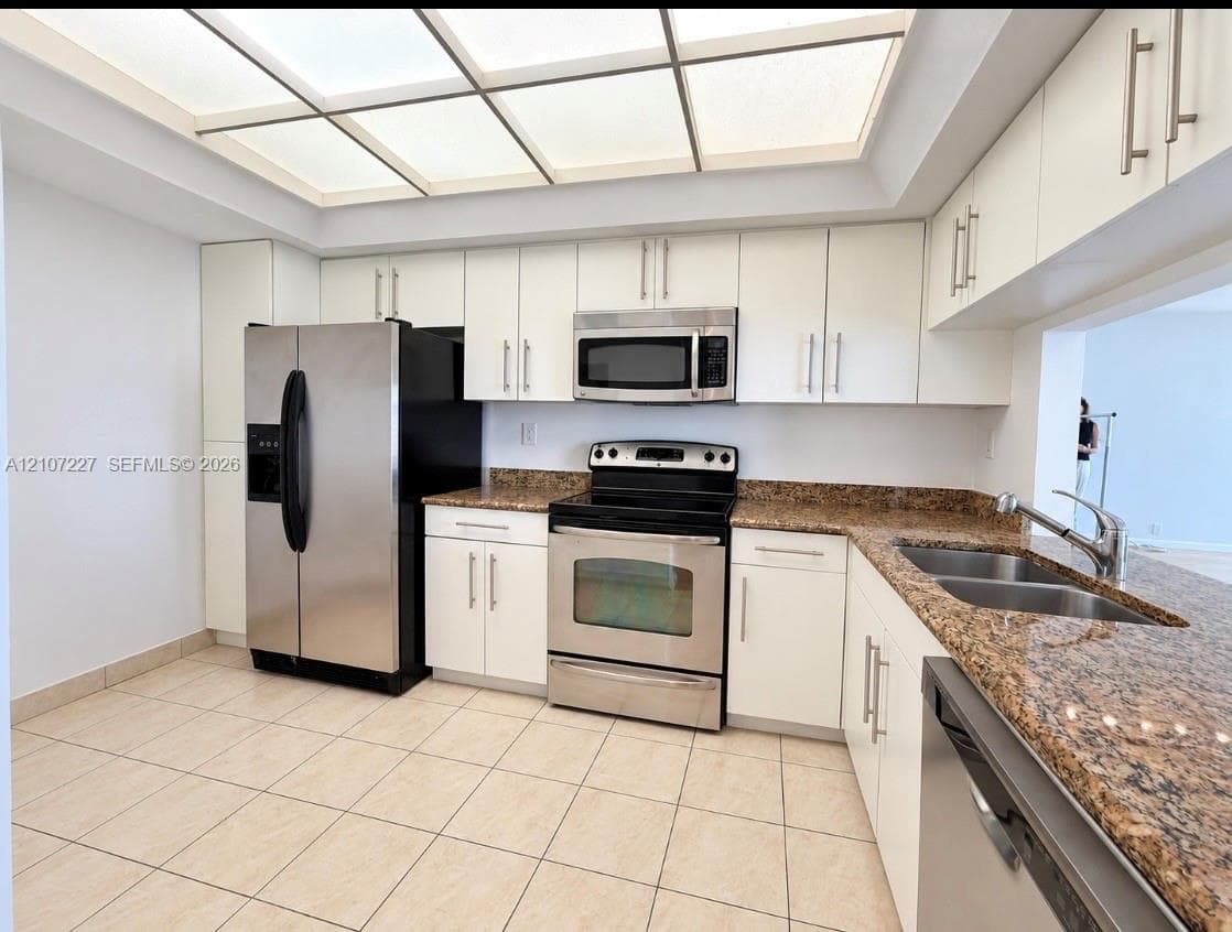 Kitchen featuring white cabinetry, stone-surface countertops, stainless steel appliances, tiled flooring, and a recessed ceiling panel