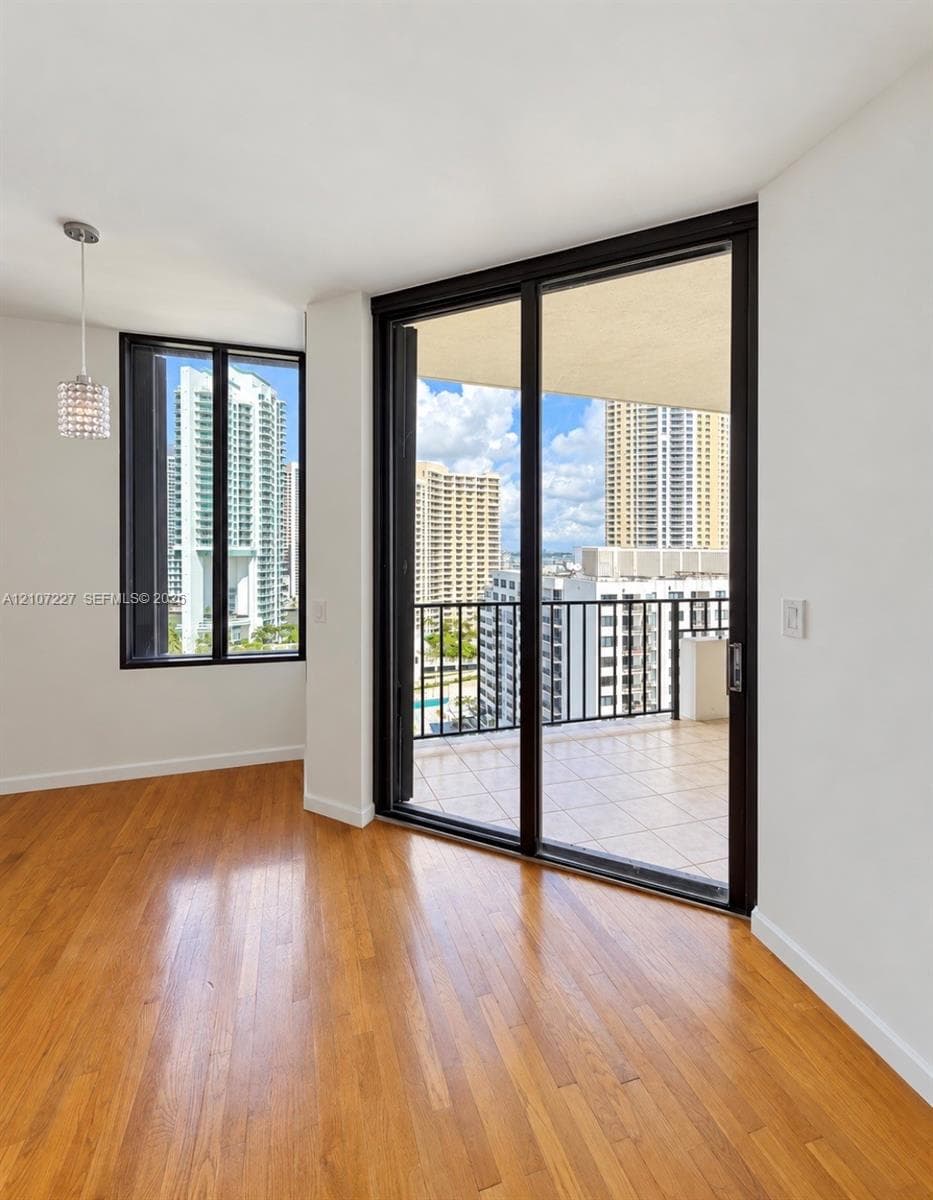 Wood-finish flooring, floor-to-ceiling glass sliding doors, private balcony with tile surfacing, and a crystal pendant light fixture
