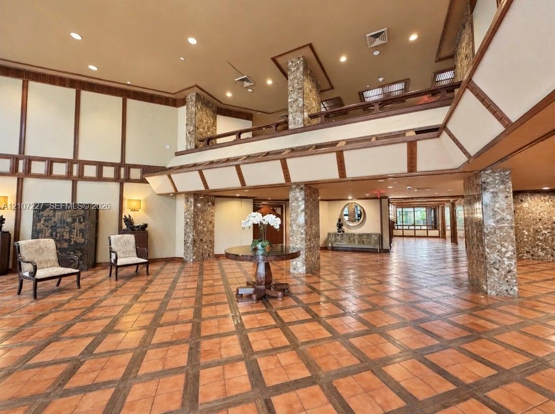 Grand foyer featuring stone-clad structural pillars, multi-level ceiling design, tile flooring with wood-inlay border, and custom wood wall trim